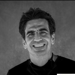 Foto em preto e branco de Roberto Levi: homem branco de cabelos escuros sorrindo para a foto.