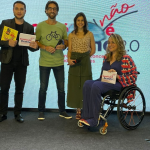 Alex Duarte (homem branco segurando livros) , Henri Zylberstajn e Débora Goldsveg de pé e convidada em cadeira de rodas.