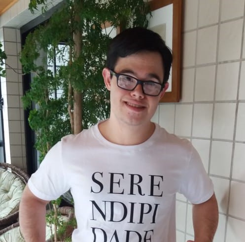 Homem branco de cabelos escuros vestindo camiseta branca com "Serendipidade" escrito em preto.