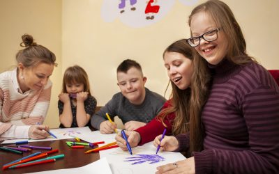 5 crianças sentadas estudando, desenhando e sorrindo.