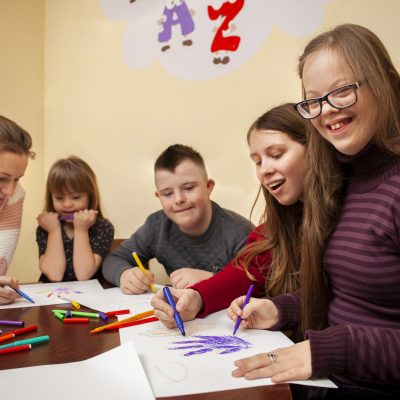 5 crianças sentadas estudando, desenhando e sorrindo.