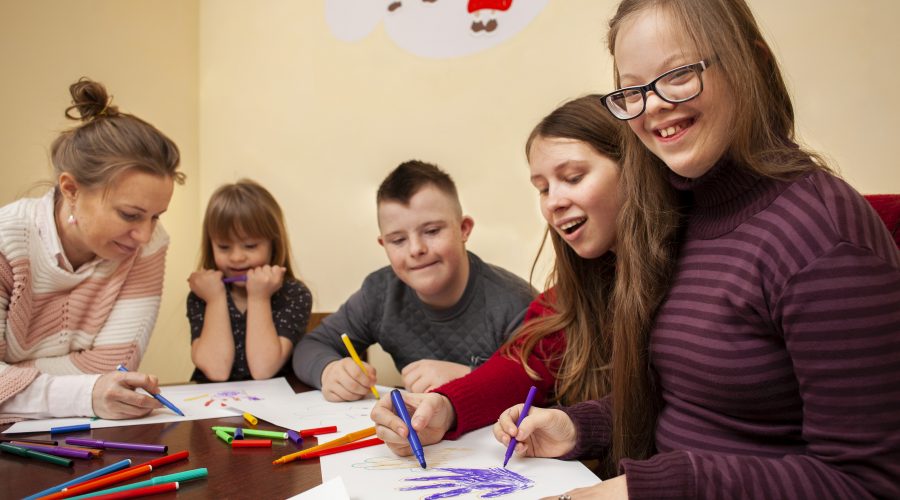 5 crianças sentadas estudando, desenhando e sorrindo.